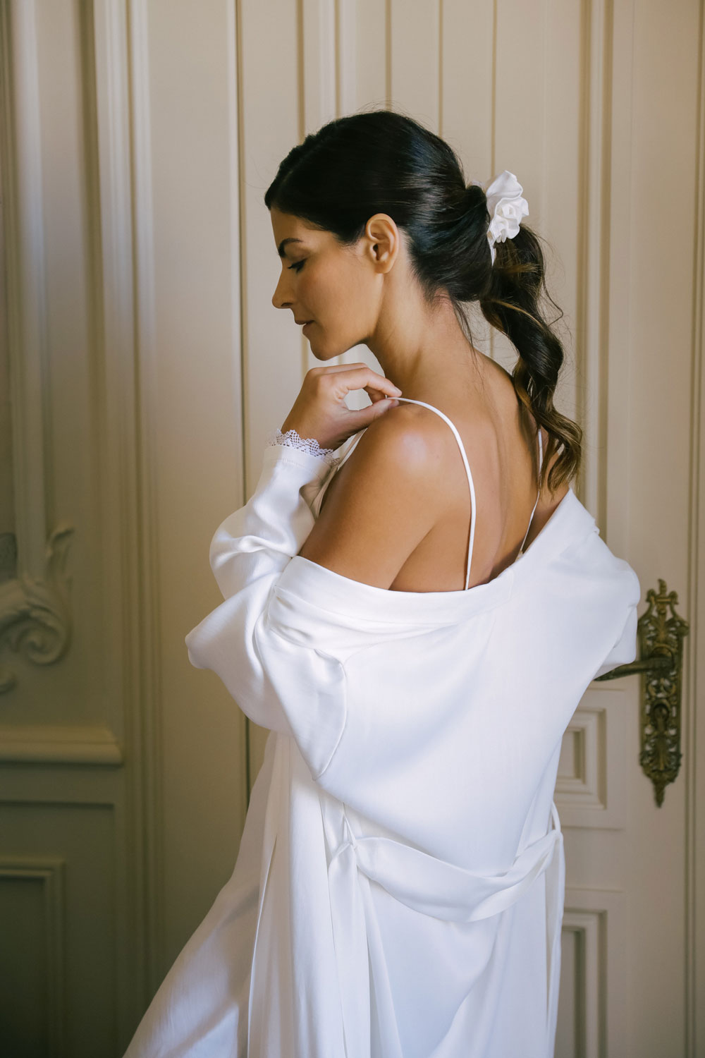 woman seen from the side adjusting the strap, showing her white silk robe from Leizi's Silky Dreams collection