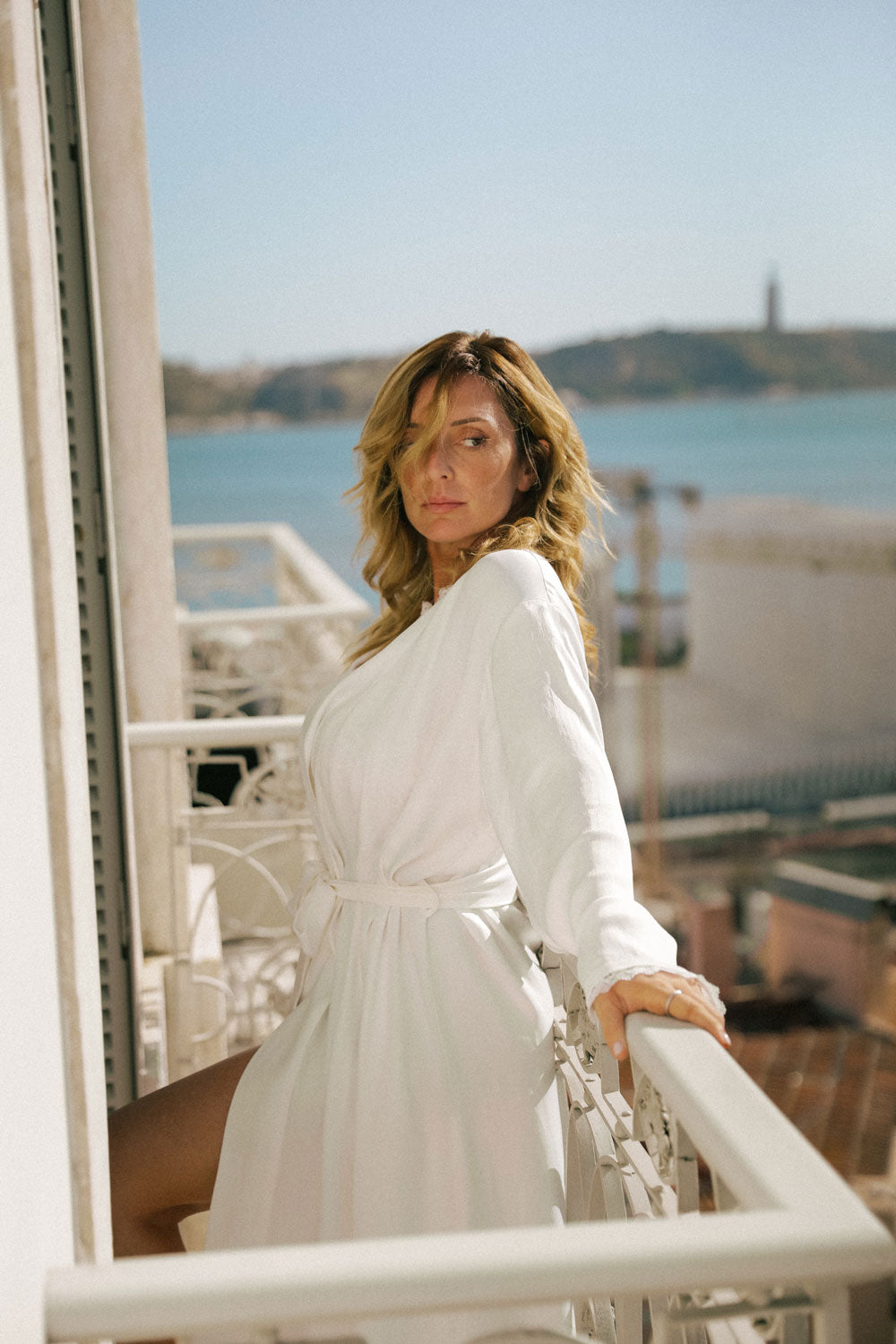 woman in confident pose on a porch, dressed in a white silk robe from Leizi's Silky Dreams collection.