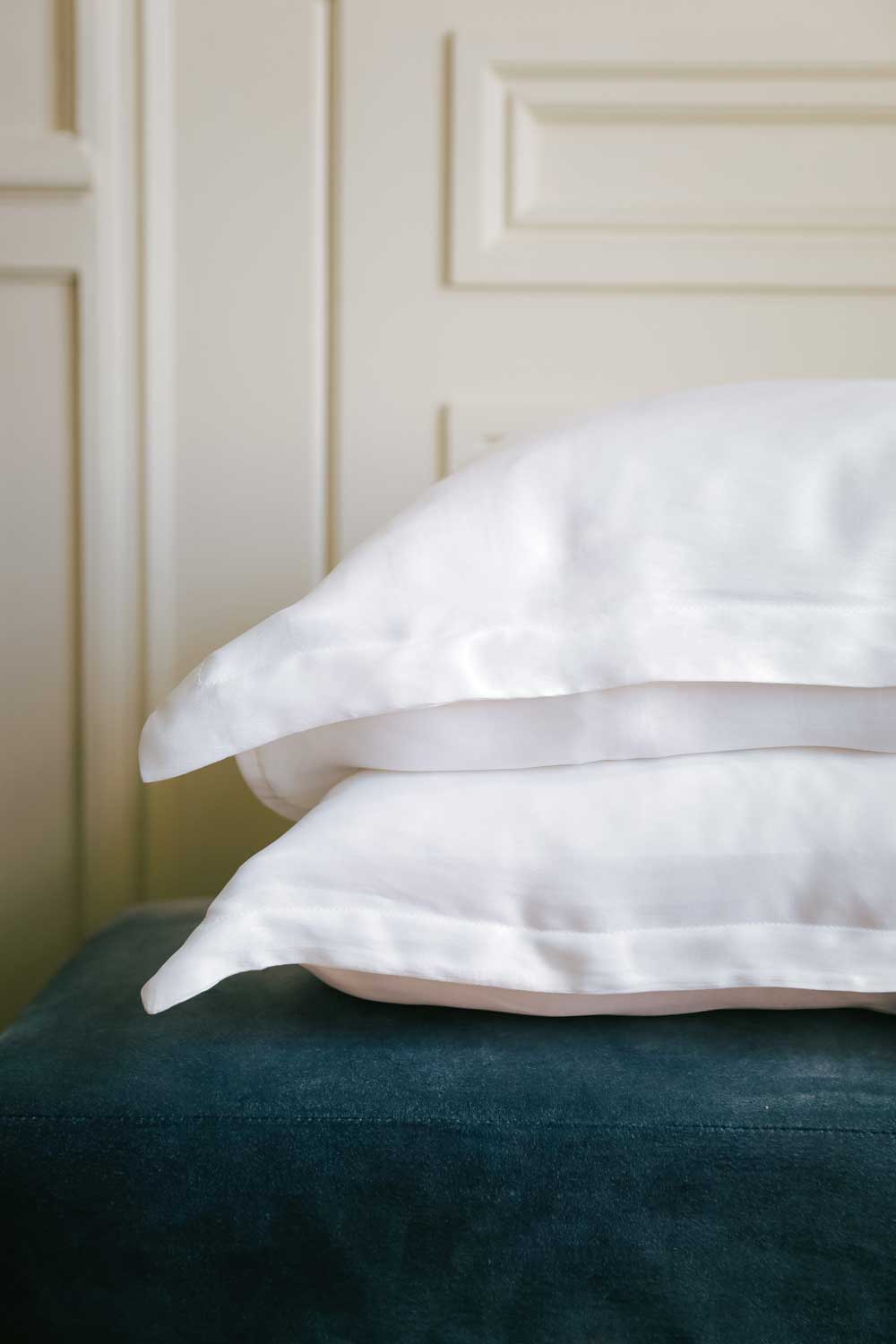 Two pillows with white pillowcases made with silk from orange peel on a blue teal velvet sofa.