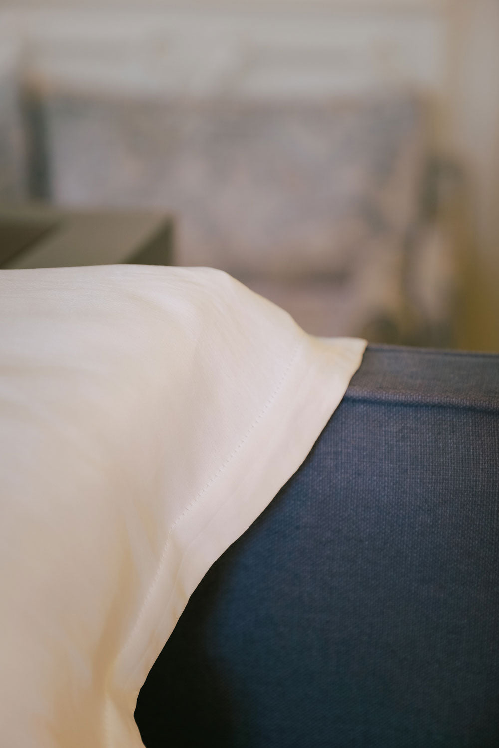 Detail of a white silk pillowcase leaning against a blue headboard.