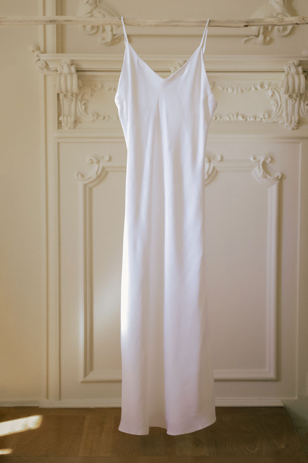 white nightdress in orange silk hanging on a wood stick, seen from the front.
